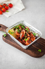 Fried shrimp with herbs and sauce on a wooden board on a light gray background