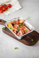 Boiled shrimp with greens on a wooden board on a light gray background