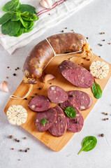 Smoked delicatessen sausage on a wooden board on a light background with pepper and garlic