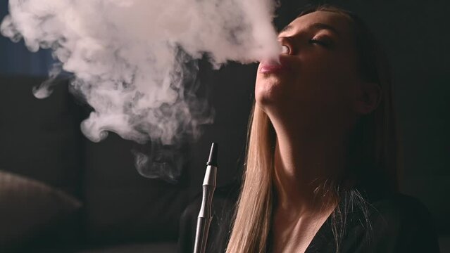 An attractive young adult woman smokes a hookah at home in anticipation of a party with her friends
