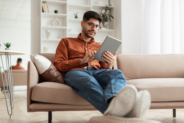 Smiling young Arab man using digital tablet at home