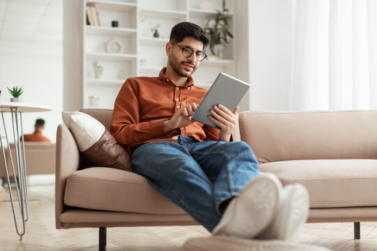 Smiling Young Arab Man Using Digital Tablet At Home