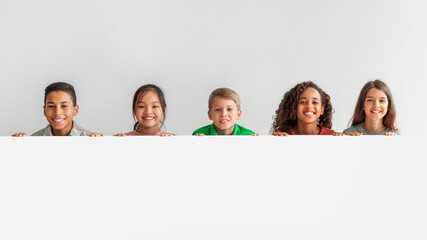 Happy Multicultural Children Posing With Empty White Poster, Gray Background