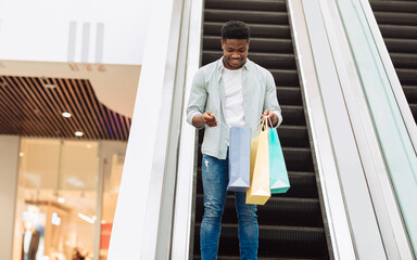 Happy black man holding shopping bags looking inside
