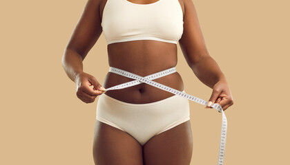 Close up crop of fat African American woman in underwear on yellow studio background measure waist...