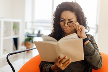 Focused black lady in glasses trying to read book