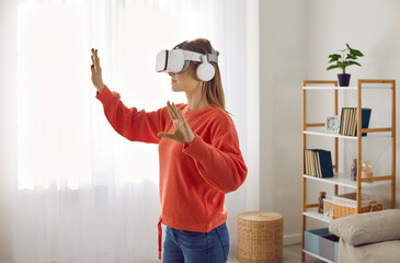 Female gamer standing in living room wearing VR headset, enjoying latest tech innovation,...