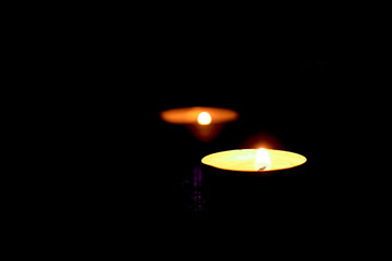 Round candles. Two lighted candles glow on a dark background.Low-light atmosphere.
