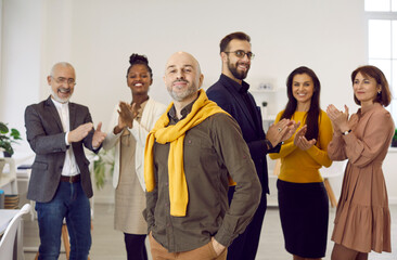 Portrait of happy proud middle-aged male employee forefront feel motivated, smiling diverse colleagues applaud on background. Multiethnic employees congratulate coworker with work promotion.