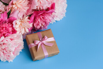 A bouquet of peonies and a gift in craft paper on a blue background. Copy space