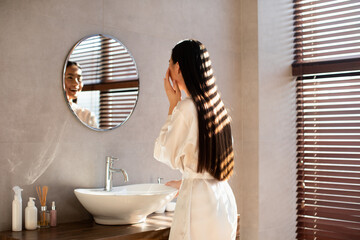 Beautiful long-haired japanese lady in bathrobe looking at mirror