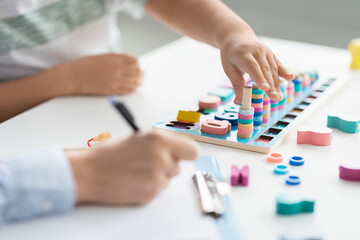 Close up of little child hands playing with logical wooden game, professional woman therapist...