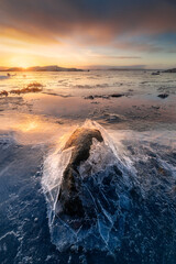 A thin layer of ice broken around a rock along the beautiful south coast of Sweden during a beautiful sunrise. Photo was taken a cold morning in winter.