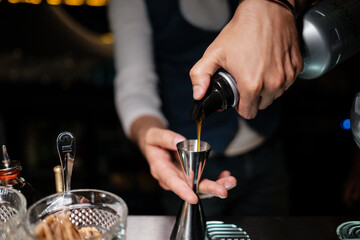 The bartender pours liquor into a jigger. A man learns how to make cocktails at the bar.