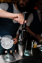 The bartender pours alcohol from a jigger into a shaker. A man learns how to make cocktails at the bar.