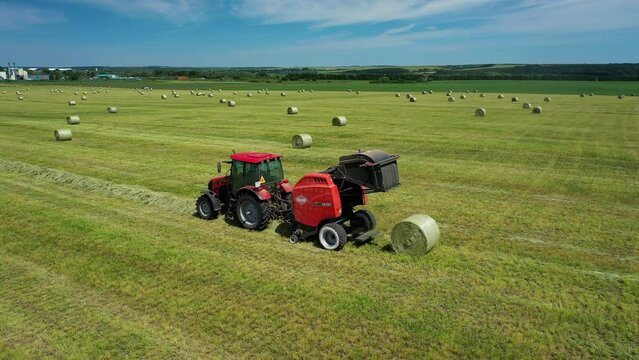 Tractor uses trailed bale machine to collect straw in field and make round large bales. Haymaking. Tractor collecting hay and making haystacks.