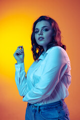 Portrait of young beautiful girl with long curly hair posing isolated on orange background in neon light, filter. Concept of emotions, beauty, fashion