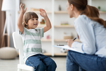 Happy emotional little boy talking to therapist at office, sharing funny story to specialist during...