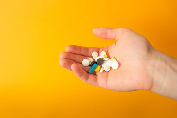 Man's palm holds a handful of different multicolored pills, capsules and drops. Yellow background. Health care concept.