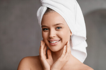 Happy lady posing with towel on head after bathing routine, standing in modern bathroom and smiling...