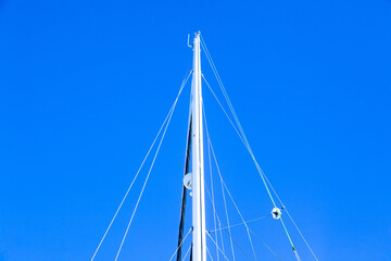 Fototapeta premium The mast of a sailing yacht with a radar, sail ropes and a folded sail, viewed from below against the sky.