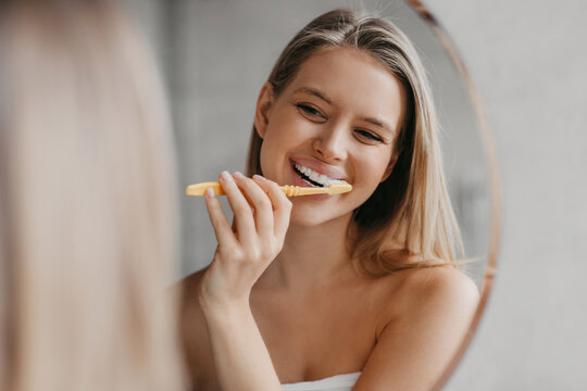 Oral hygiene, healthy teeth and care. Young woman brushing teeth with toothbrush and looking in mirror in bathroom
