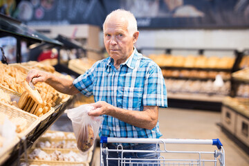 old age senor examines bakery products in the grocery section of the supermarket