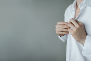 A man fastens the buttons of a white shirt on the background of the wall