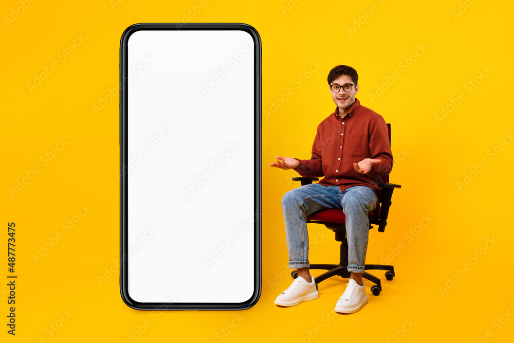 Poster man sitting near huge phone empty screen over yellow background
