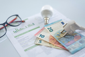 a white electric cap, euro banknotes, light bulb and glasses on an electric bill, . Rising cost of electricity . Payment of electricity bills. Increasing the concept of electricity prices.