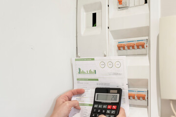 a hand holding an electricity bill and calculator in front of power control switch, concept of electricity price increase