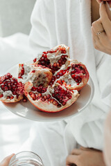 A girl in a white coat tastes a juicy red pomegranate
