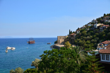coastline with ancient fortress and houses among trees and blue sea with ship and boats, Alanya