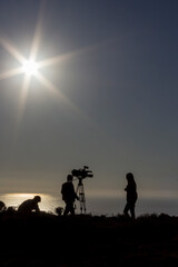 A team of reporters covering a news story outdoors. People unrecognizable when backlit.