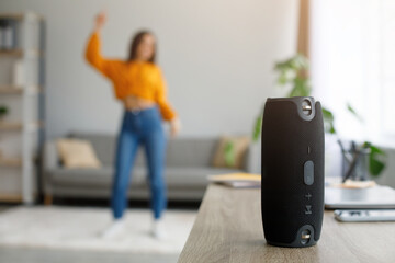 Millennial woman dancing to favorite music at home, selective focus on portable wireless speaker, free space