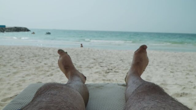 Man's legs on a deck chair on a sandy beach. The guy is sunbathing on the seashore. The guy is enjoying the sea. Hairy male legs.