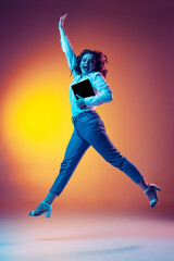 Full-length portrait of happy young beautiful girl with long curly hair jumping isolated on orange...