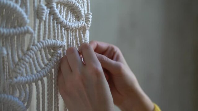 Closeup hands of freelancer woman working on half-finished macrame piece, weaves lamp shade for chandelier. Women hobby.