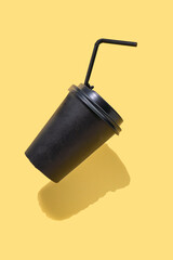 Paper coffee container with black lid on yellow background. Vertical photo