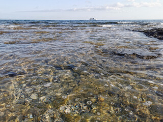 The Mediterranean Sea, in which a white pleasure yacht floats against a blue sky with clouds.