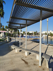 Protaras. Famagusta area. Cyprus. Promenade with a bench and a sunshade, going along the Mediterranean coast to the beach. © Elena