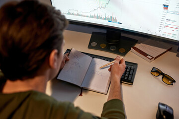 Male trader drawing business graph in notebook