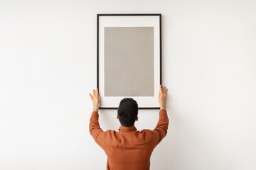 Young man hanging picture frame on the wall