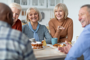 Multiracial group of positive elderly people drinking tea with cake