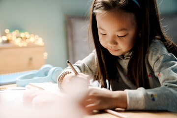 Asian girl writing in exercise book while doing homework at table