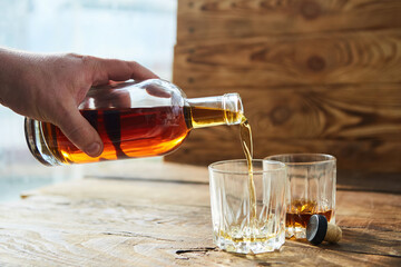 A man's hand pours an alcoholic drink cognac or whiskey from a glass bottle into a glass.