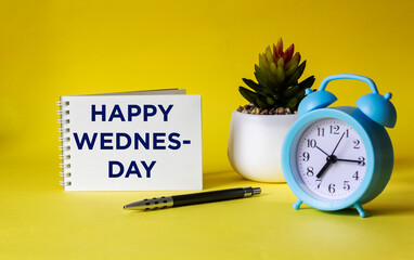 Notepad with text Happy Wednesday on yellow background with clock.