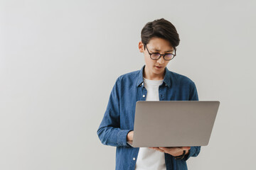 Asian brunette boy wearing eyeglasses working with laptop
