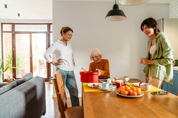 Mature women giving gift while having birthday dinner in kitchen