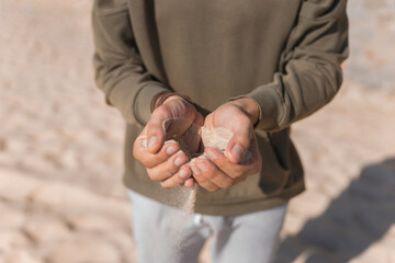 Man holding white sand in his hands. Male palms with the sand on the beach.